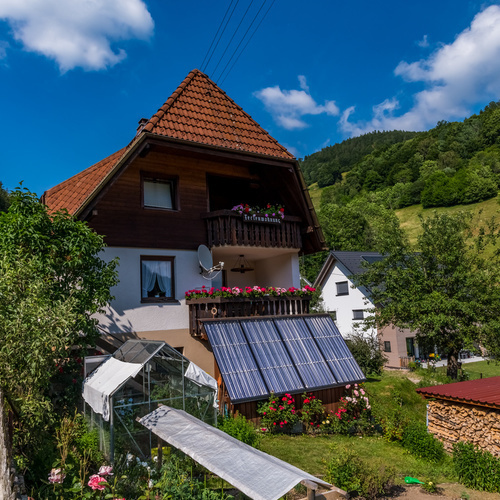 Außenansicht des Haus Christel im Vordergrund ein Gartenbereich mit blühenden Rosen und Gewächshaus - Außenansicht des Haus Christel im Vordergrund ein Gartenbereich mit blühenden Rosen und Gewächshaus -