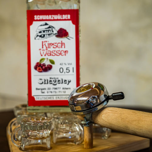 Schnapsgläser auf einem Brett mit Radklingel im Hintergrund eine Flasche Kirschwasser - Schnapsgläser auf einem Brett mit Radklingel im Hintergrund eine Flasche Kirschwasser -